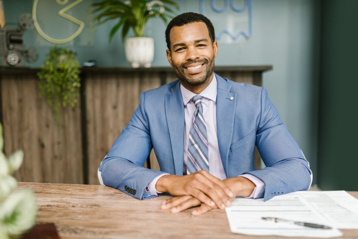 An accountant in a blue jacket smiling at a desk with paperwork and a pen