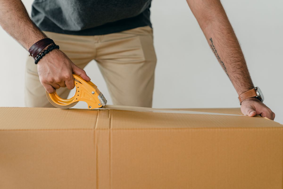 A seller sealing a large cardboard box with a yellow tape gun
