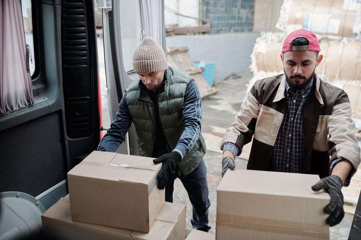 Two workers loading cardboard parcels into the back of a delivery van