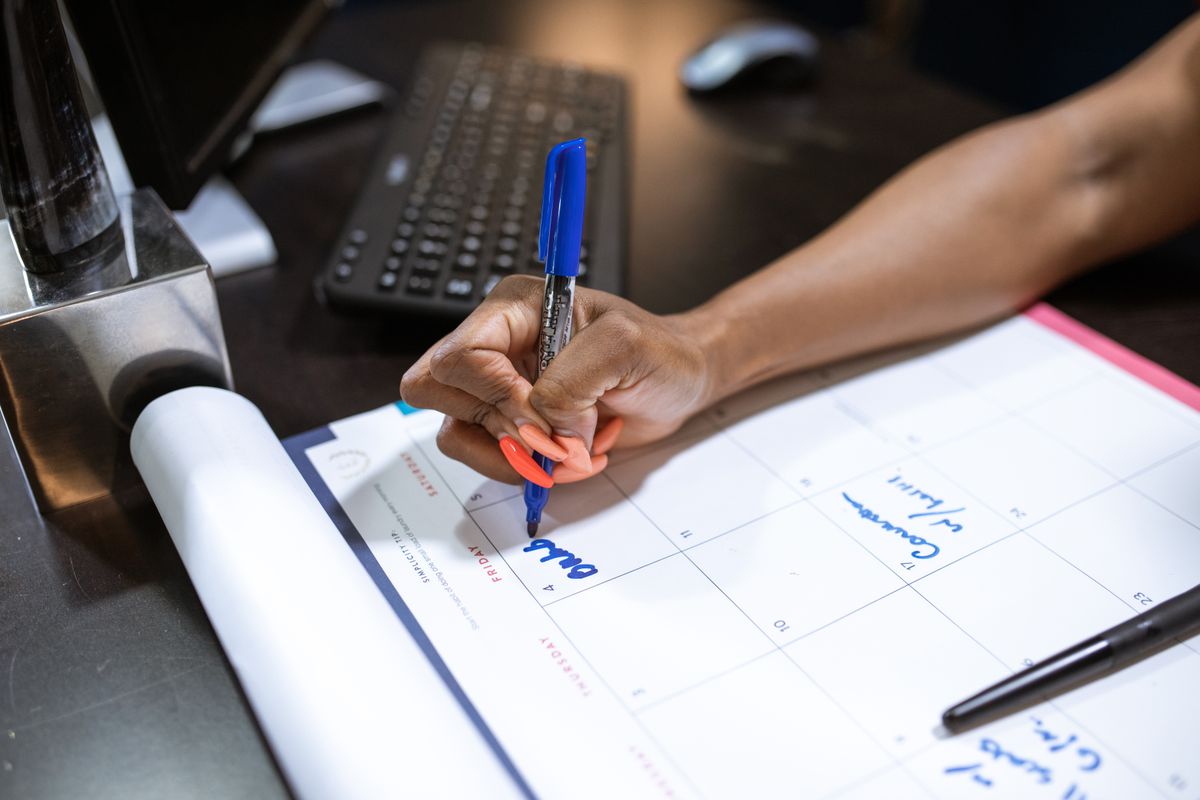 A hand writes a booking into a desk calendar with a blue marker