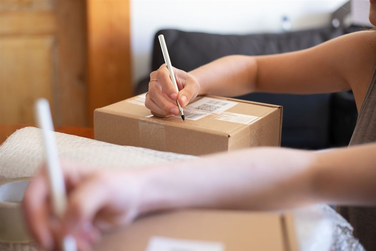 Hands labelling a small cardboard parcel for shipping