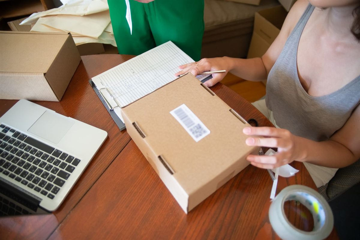 An online shop team checks an order list beside packed parcels and a laptop