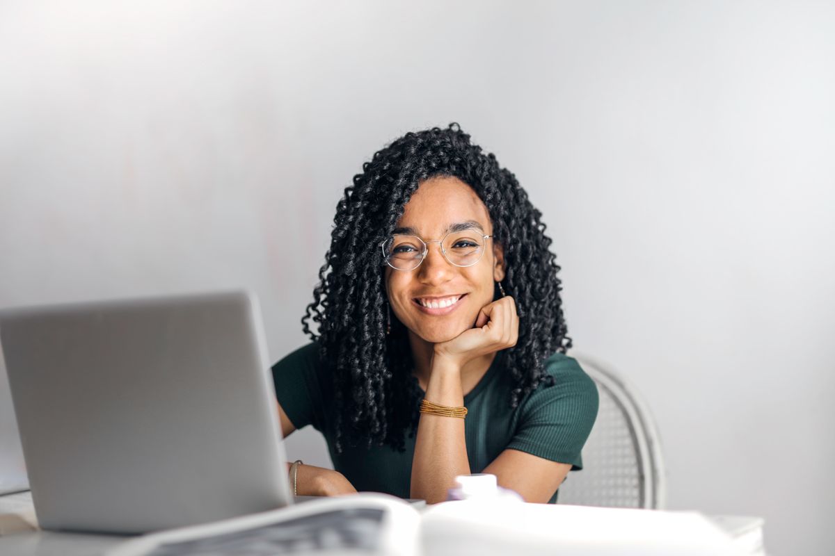 A woman with glasses sits calmly at a laptop, resting her chin on her hand while writing a reply