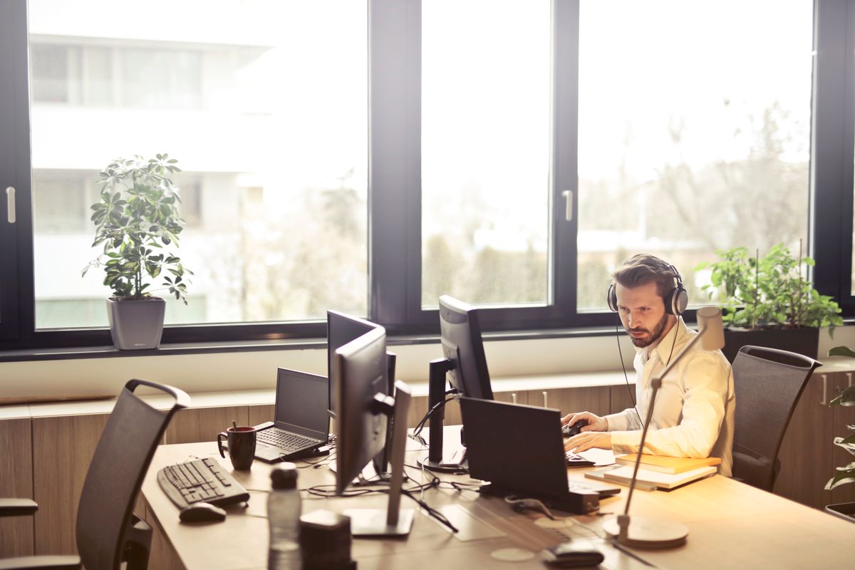 A man wearing a headset answers customer messages at a bright office desk with several monitors