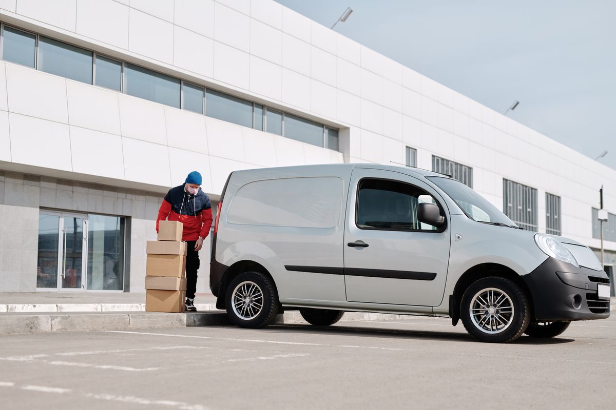 A courier unloading parcels from a delivery van outside a building