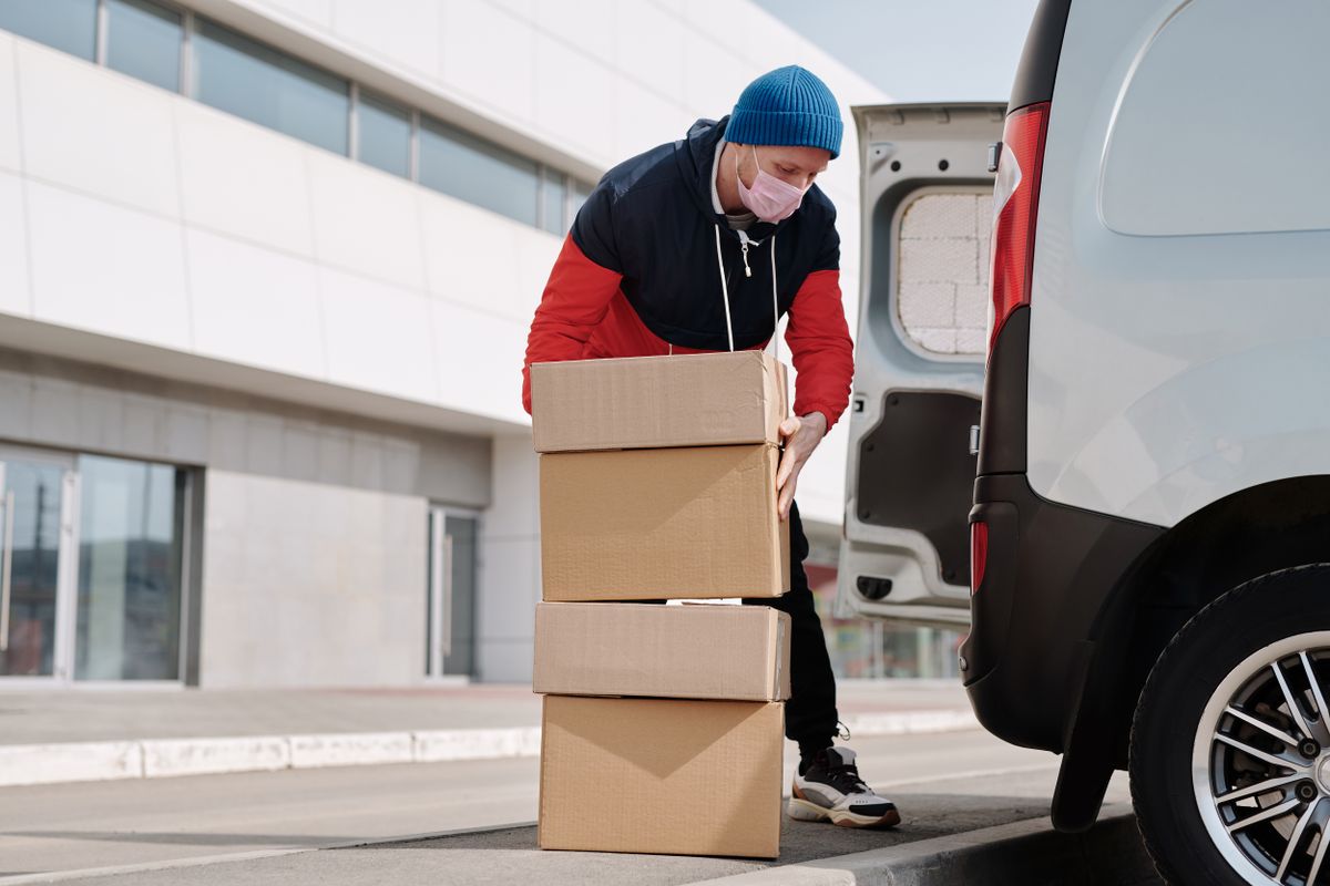 A courier stacks cardboard parcels at the open rear doors of a delivery van