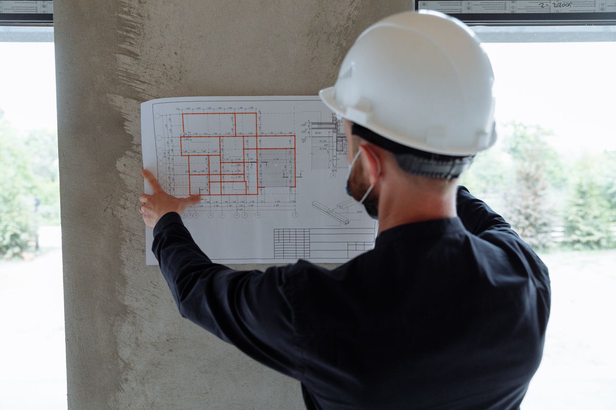 An engineer in a hard hat checks a floor plan pinned up on site