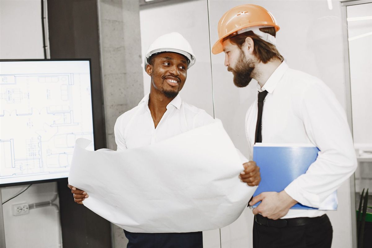 Two builders in hard hats review plans for a client project
