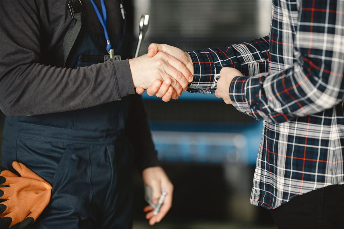 A tradesman in overalls shakes hands with a client in a workshop