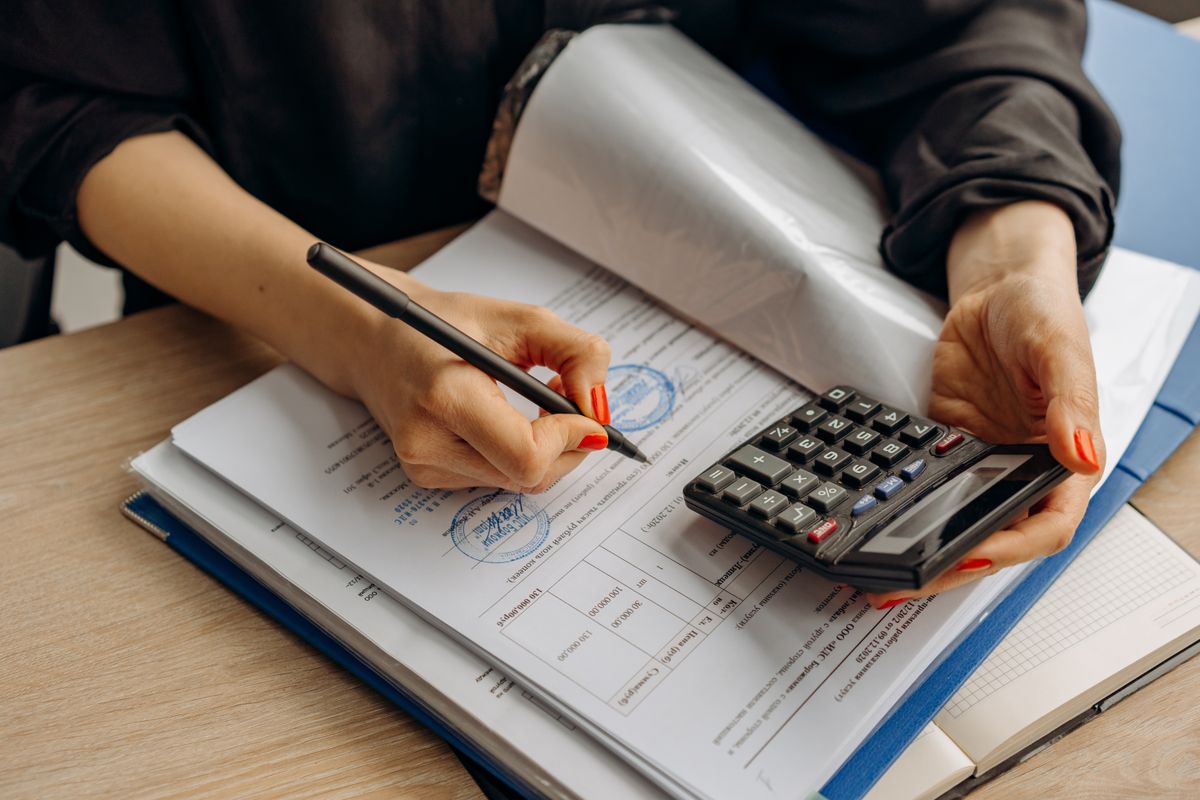A person checking figures on a stamped invoice with a pen and a calculator