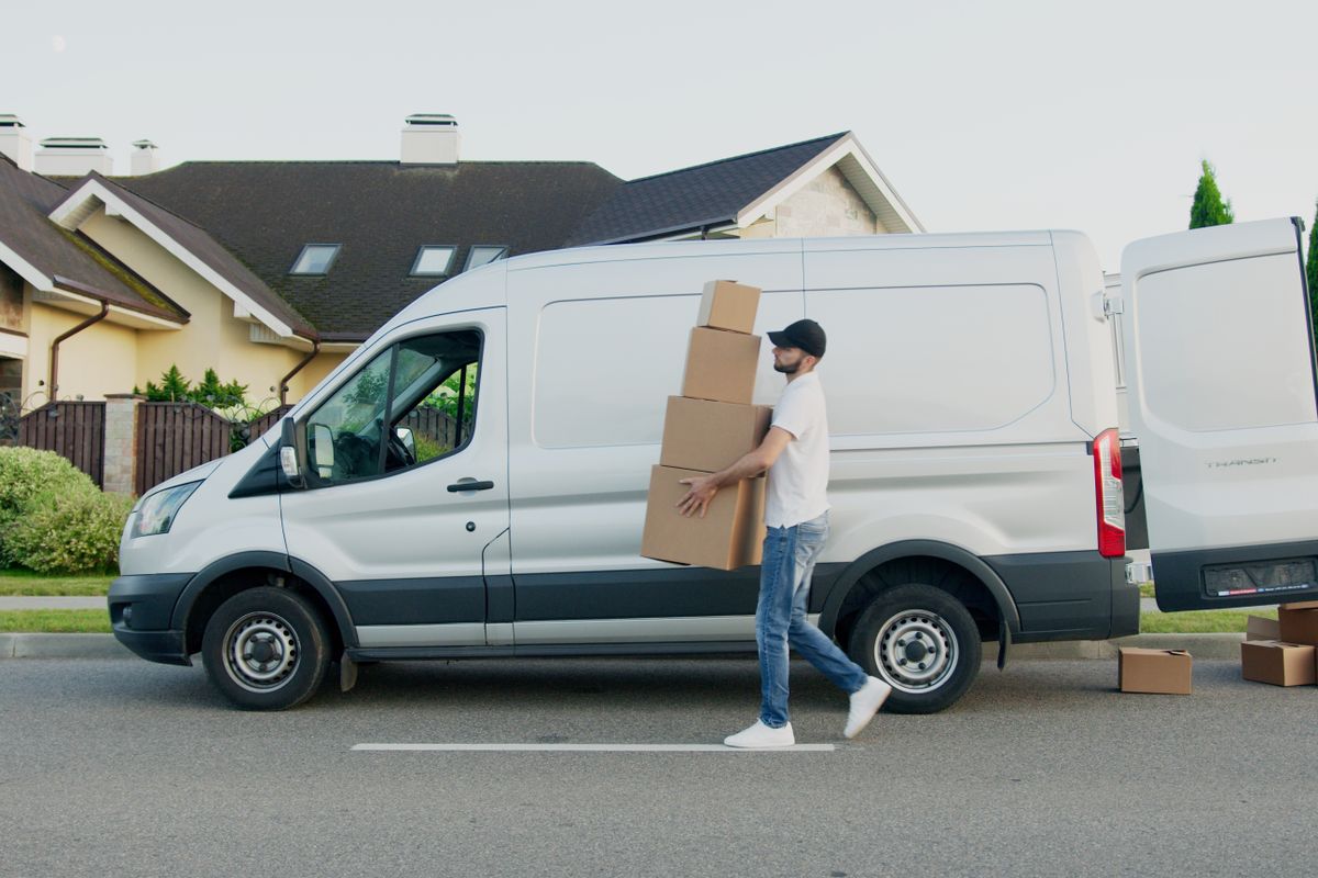 A seller loading a stack of cardboard parcels into a delivery van outside a house