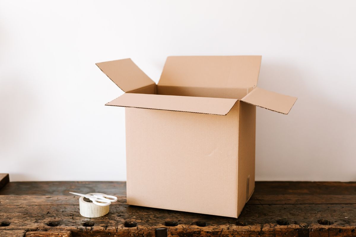 An open cardboard box with packing tape and scissors on a wooden workbench, ready for an eBay order