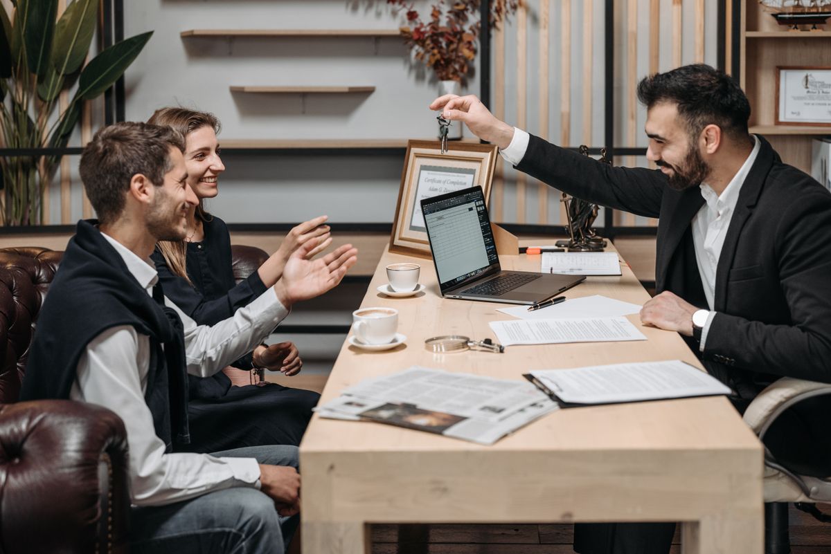An estate agent handing house keys to a smiling couple across an office desk