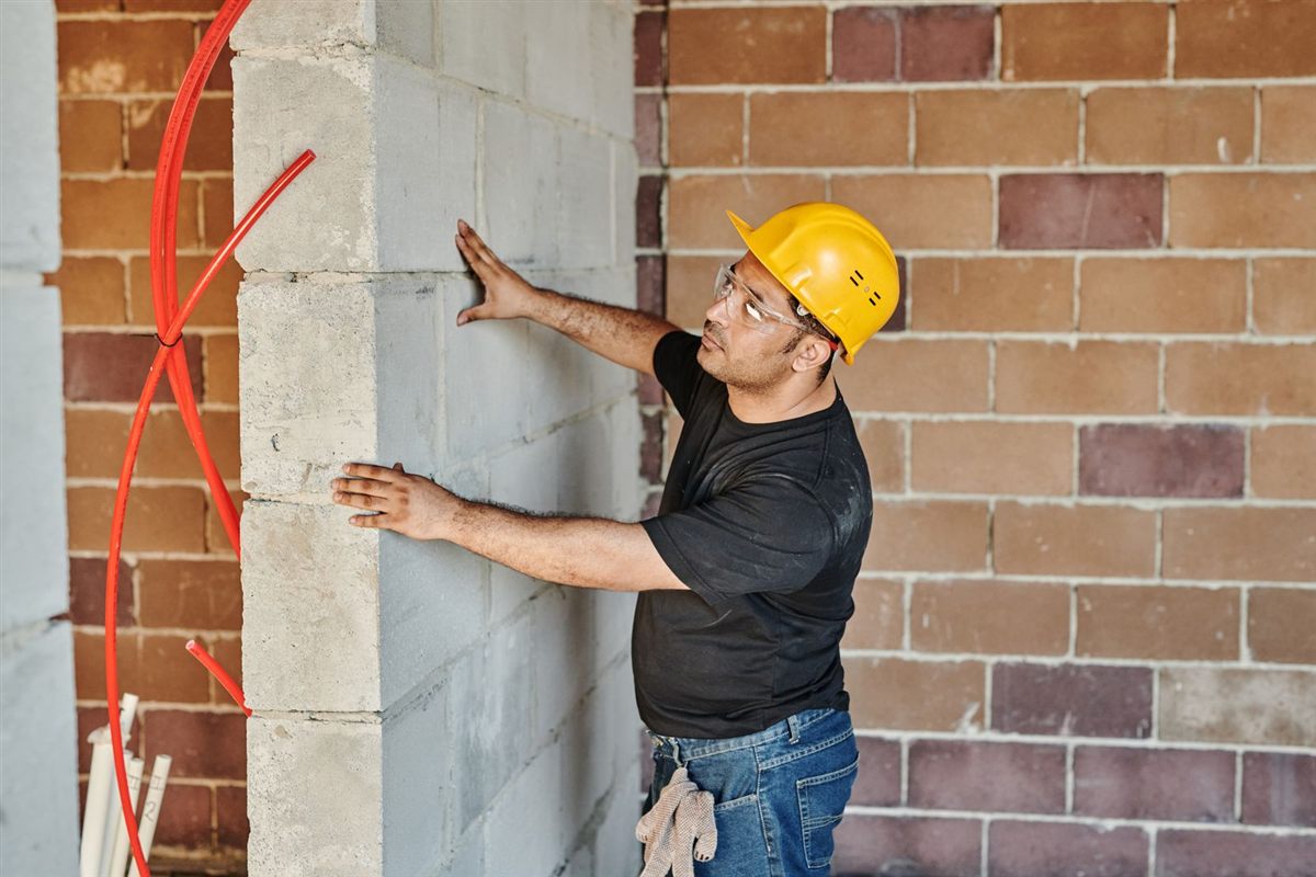 A builder in a hard hat inspects a block wall during a renovation