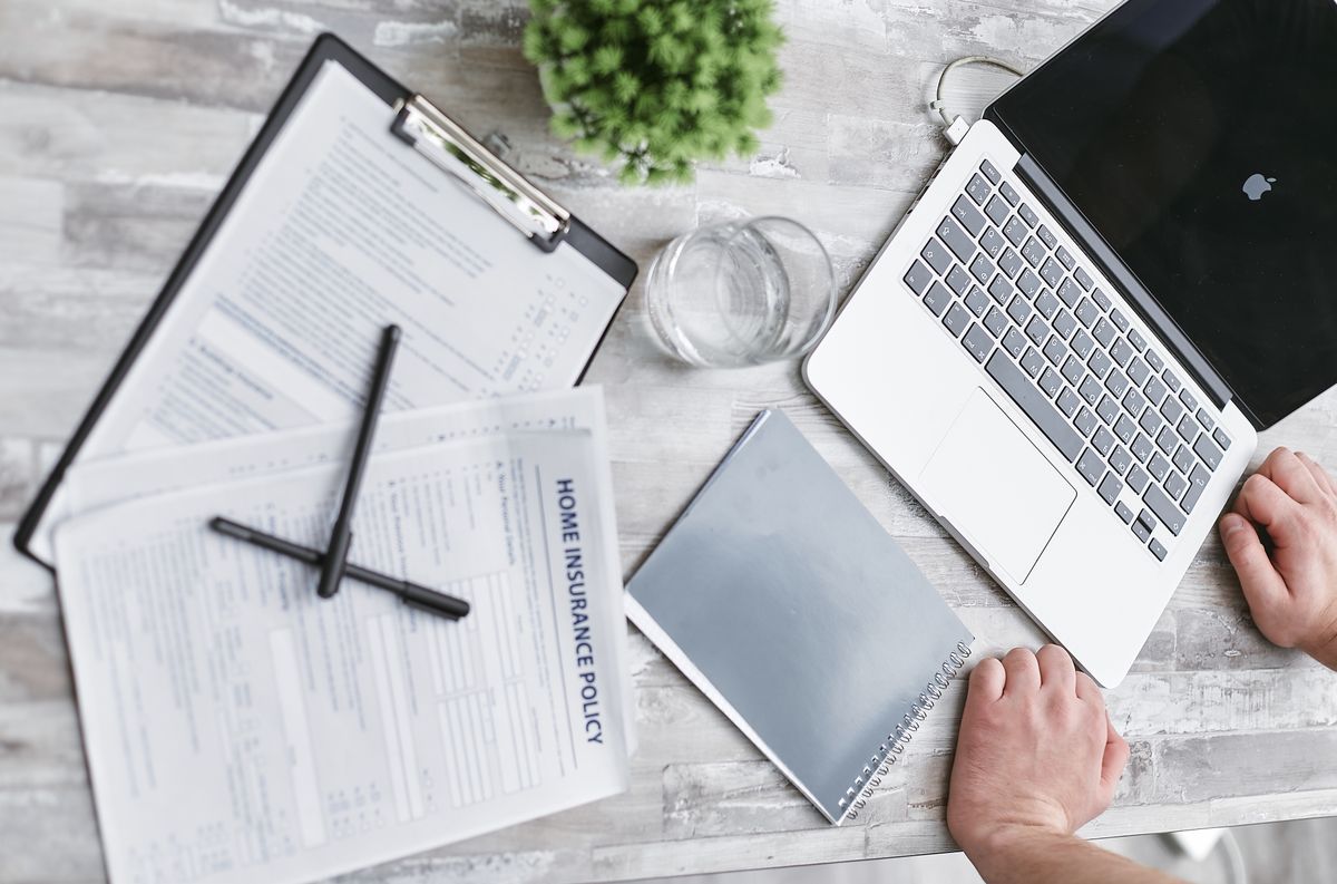 Insurance forms, a laptop and documents laid out on a desk, seen from above