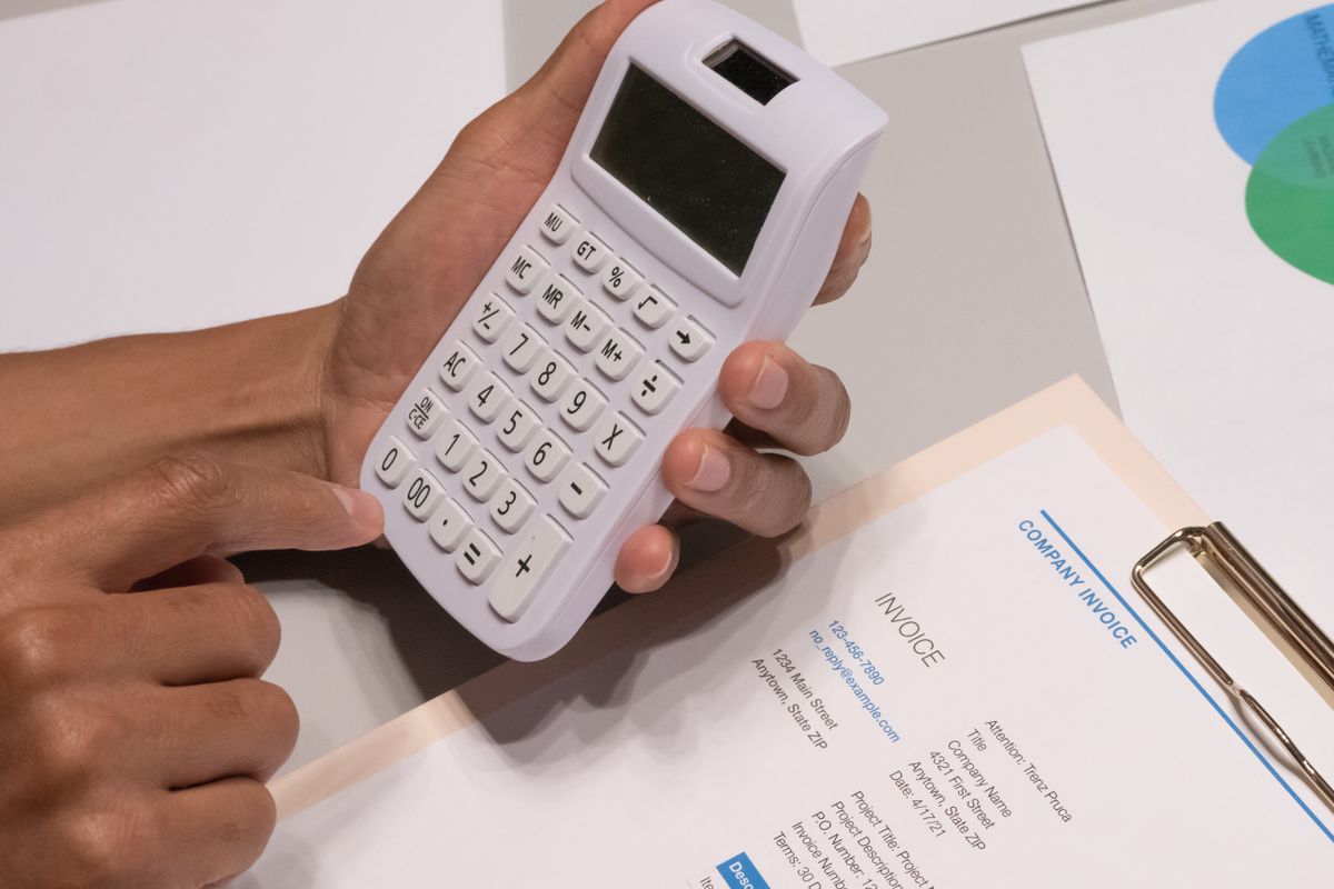 Hands working a calculator beside a printed company invoice