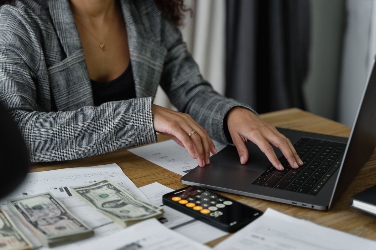 A business owner reconciling payments at a laptop with paperwork and a calculator on the desk