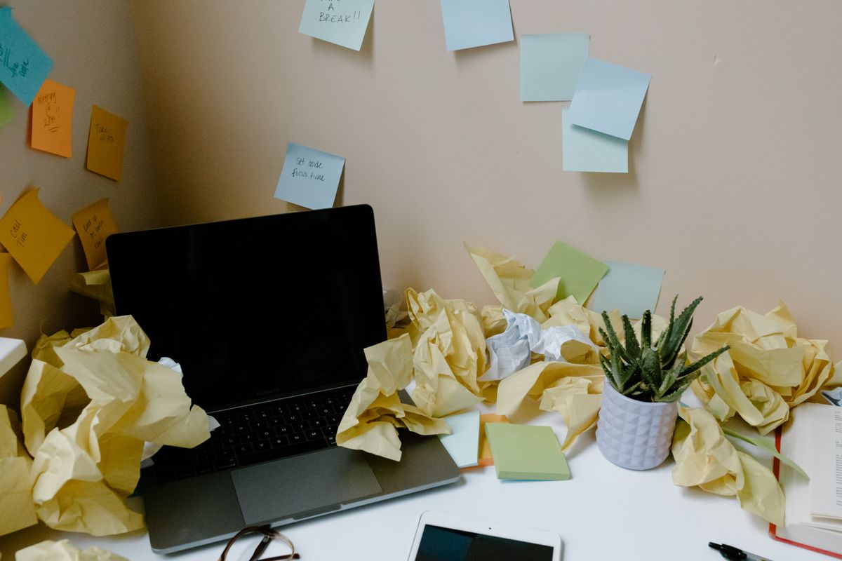 A desk buried under crumpled notes and sticky reminders around a laptop