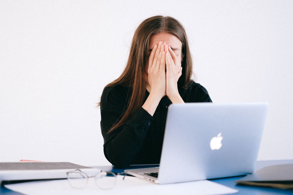 A woman at a laptop with her hands over her face, buried by the inbox