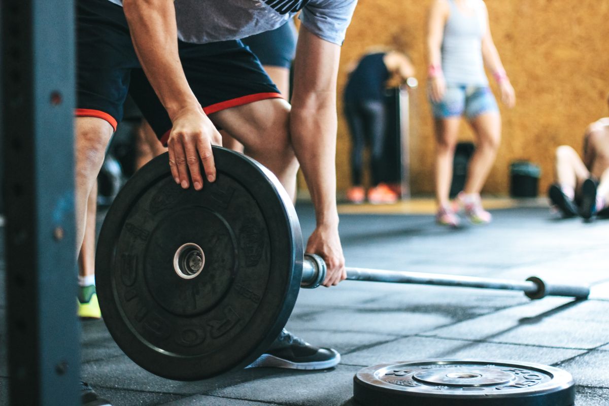 A member loading a black bumper plate onto a barbell in a busy gym