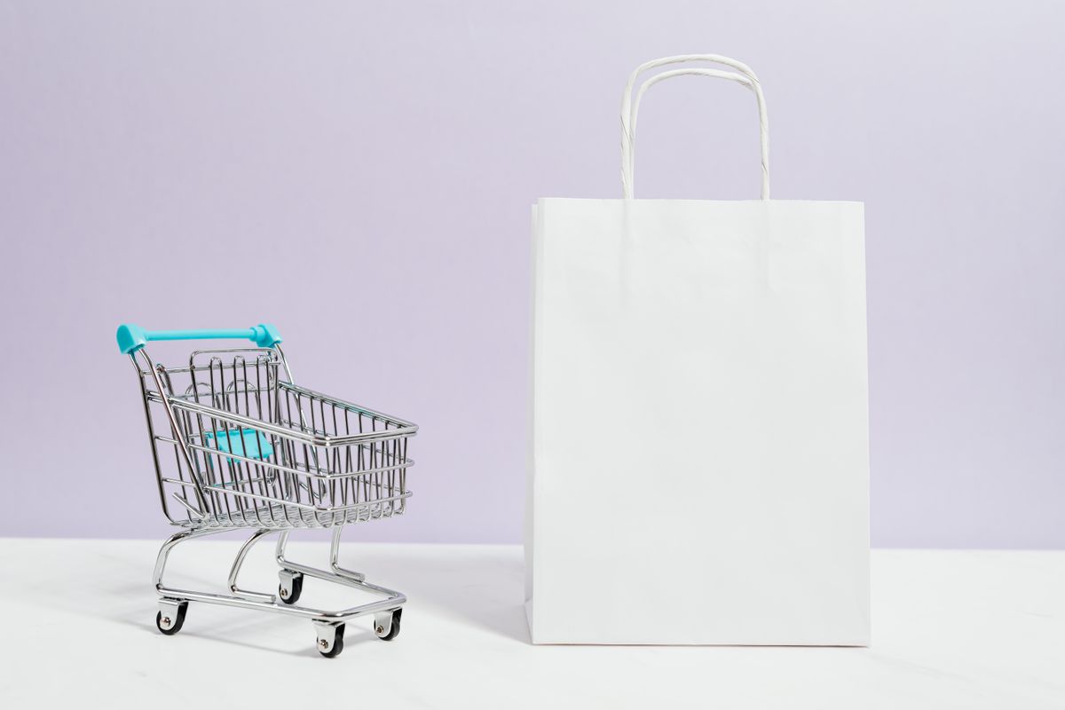 A miniature shopping trolley beside a plain paper shopping bag