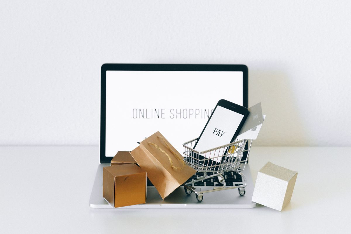 A laptop showing an online shop beside small parcels and a miniature trolley