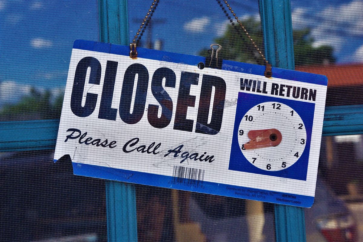A closed sign with a will return clock hanging on a shop door