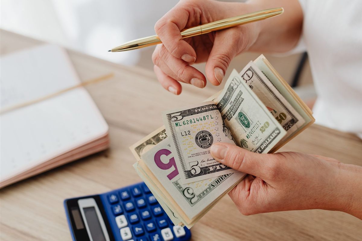 A person counts banknotes over a desk with a calculator and receipts