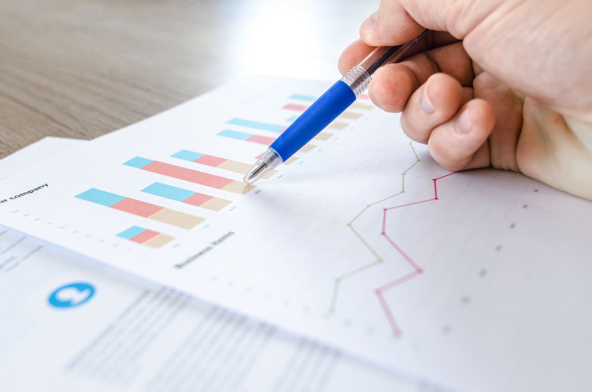 A hand with a pen works through printed pricing charts on a desk