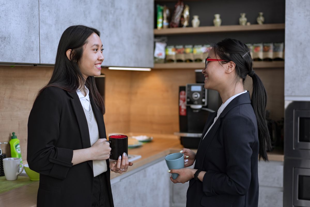 Two colleagues chatting happily over coffee in an office kitchen