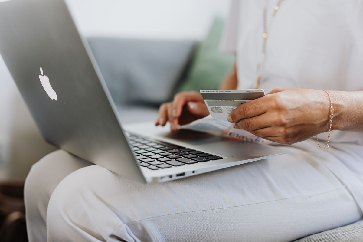 A customer sits on a sofa with a laptop, holding a bank card while dealing with an online order