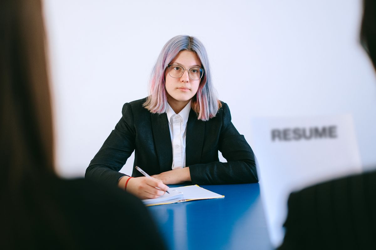 A young woman in a suit writes notes at a table during a job interview
