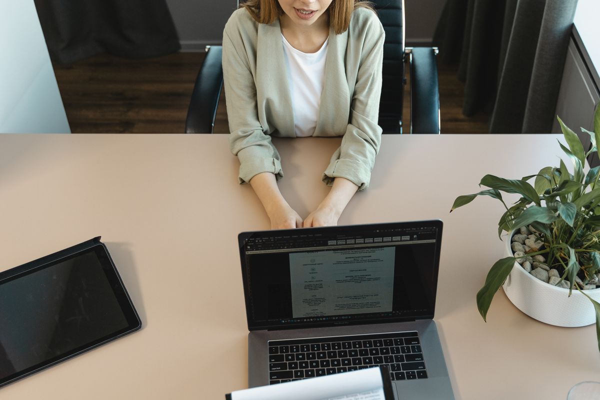 A high-angle view of a candidate sitting across a desk from an interviewer's laptop in a bright office