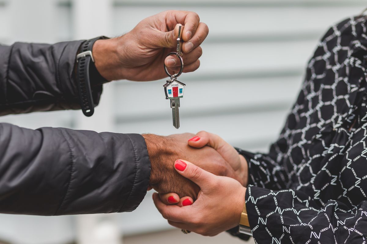 A landlord hands over a house key while shaking hands with a tenant