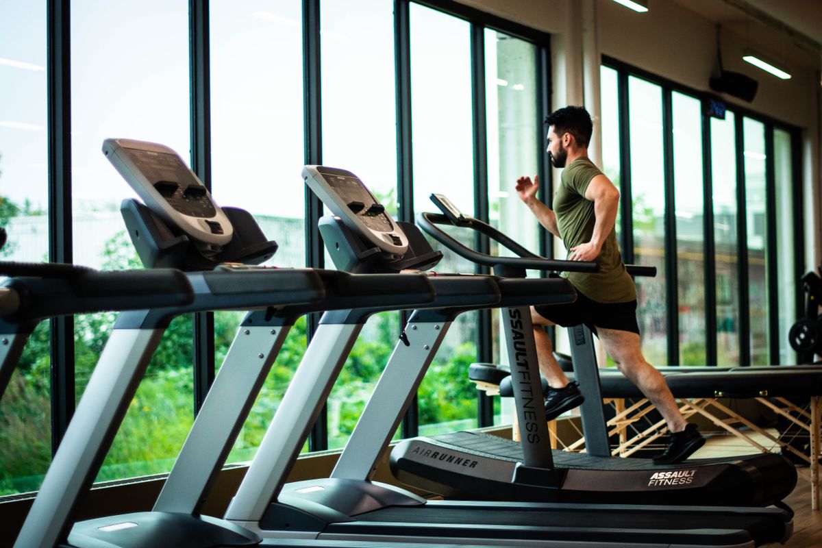 A member running on a treadmill beside tall windows in a bright gym