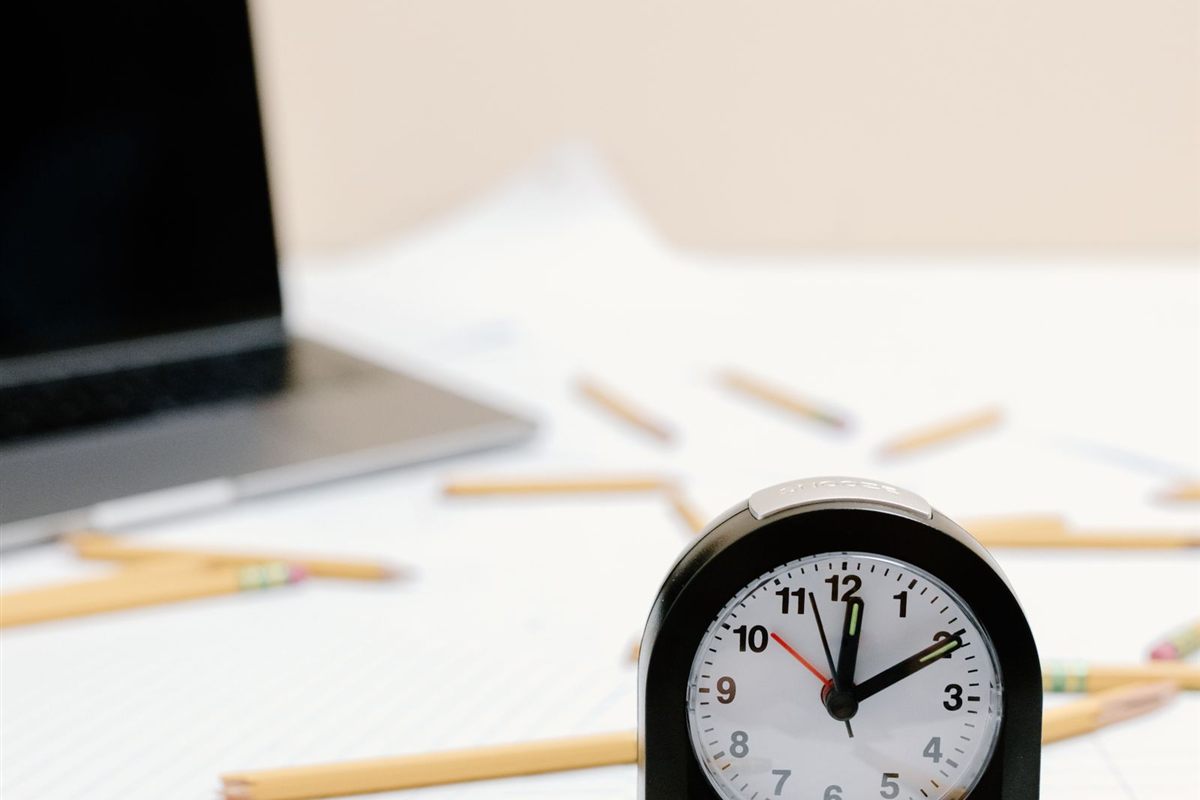 An alarm clock stands on paperwork among scattered broken pencils