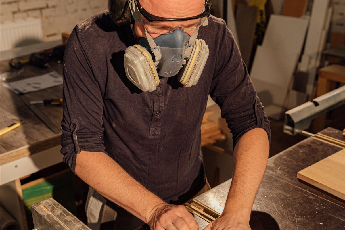 A craftsman in safety gear works a table saw in a busy workshop