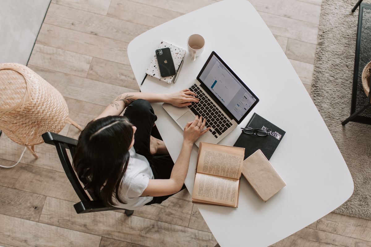 Overhead view of a person composing an email at a laptop with a notebook and coffee on the desk