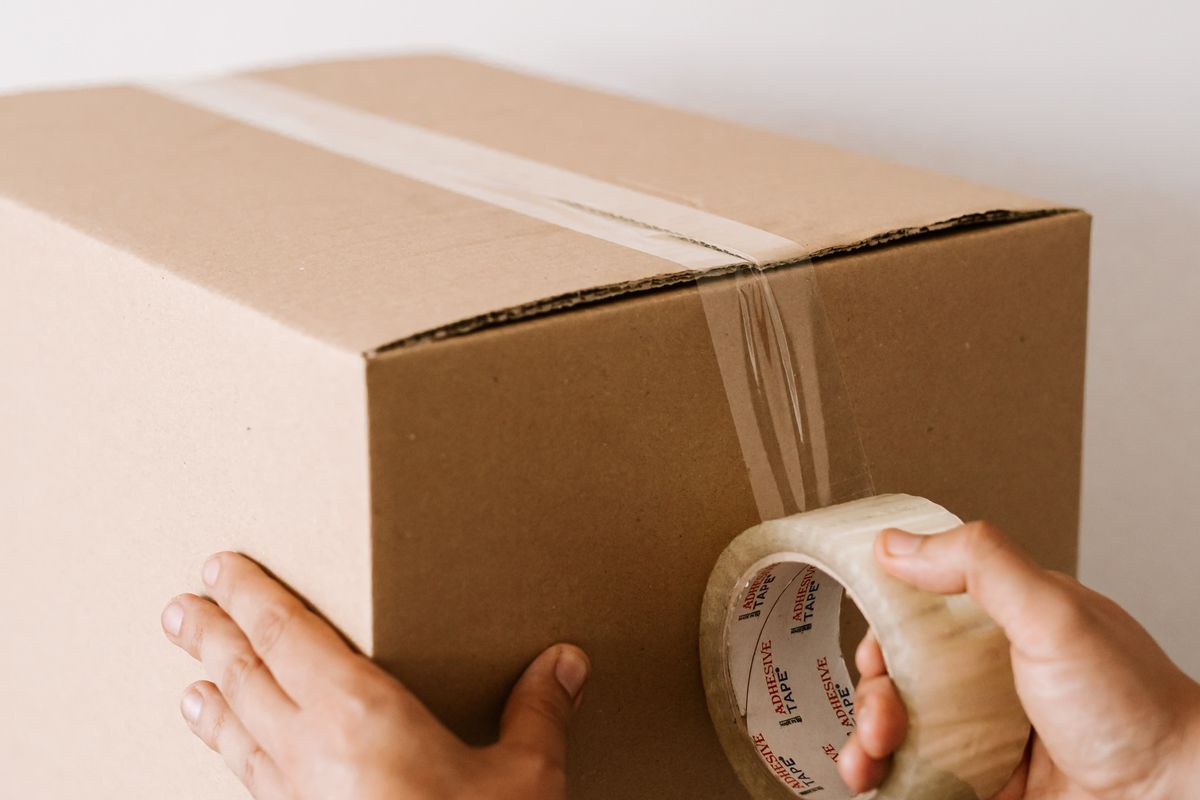Hands sealing a cardboard parcel with packing tape