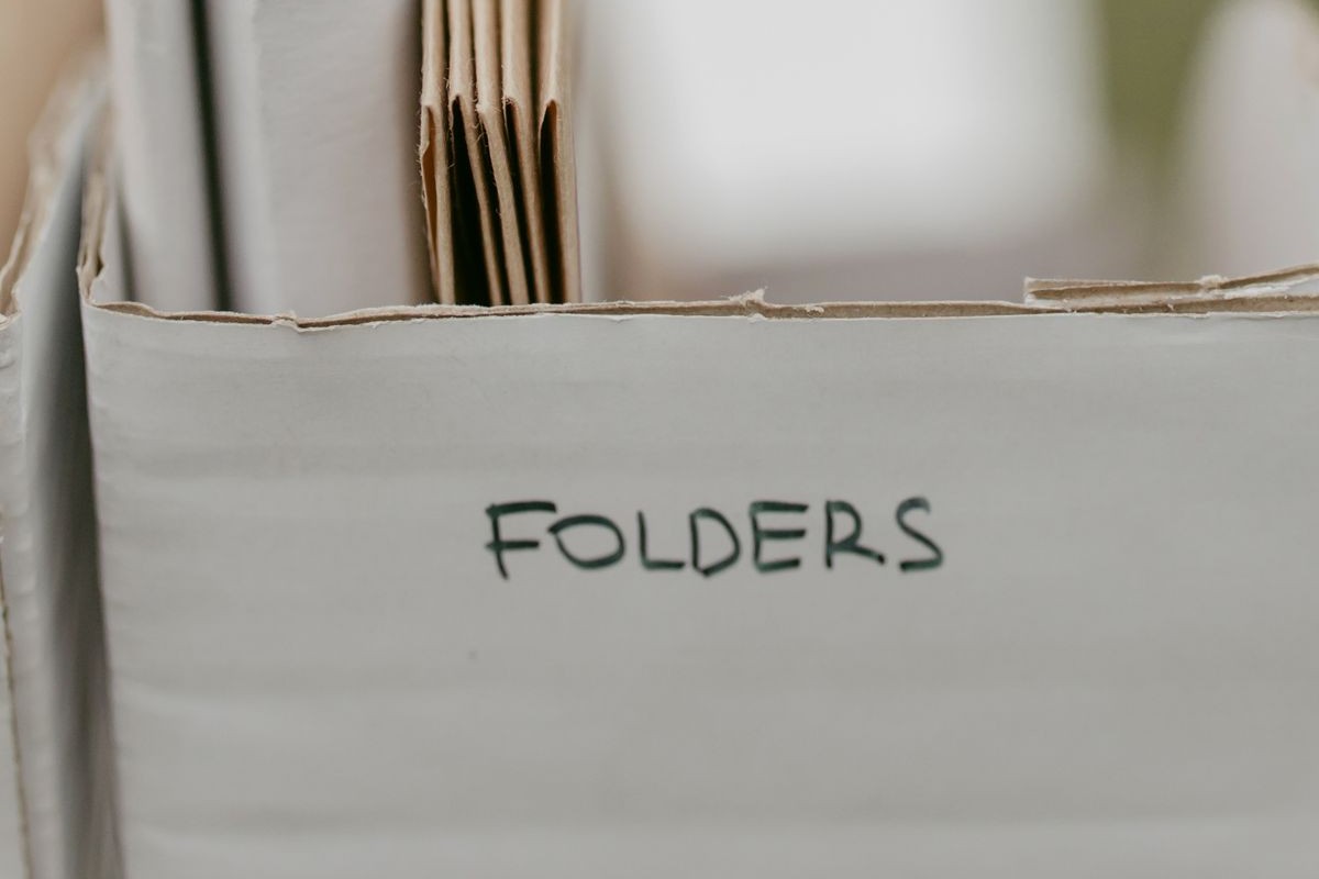 A cardboard storage box of paper folders with the word Folders written on the front in marker pen