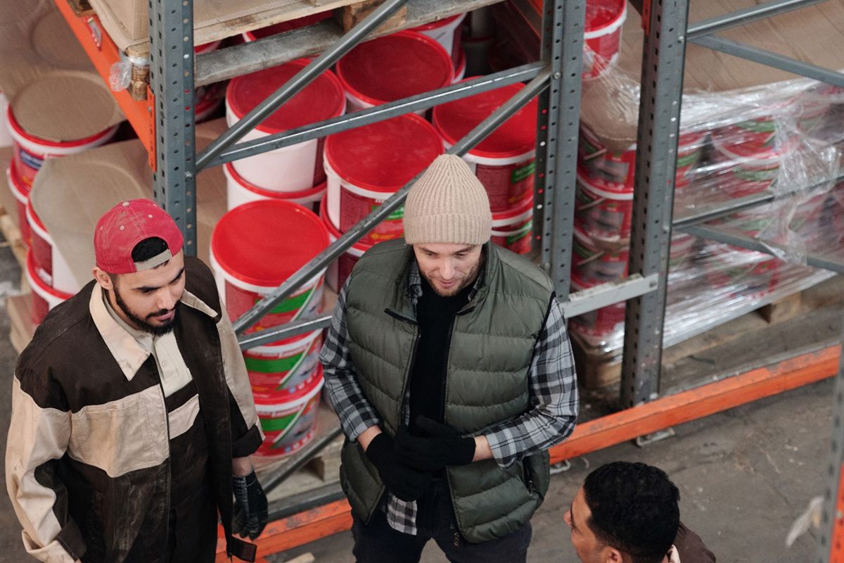 Warehouse workers discuss stock beside tall racking