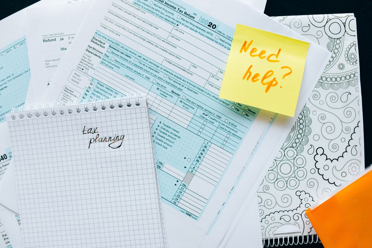 Tax forms and a notebook marked tax planning with a sticky note that says need help