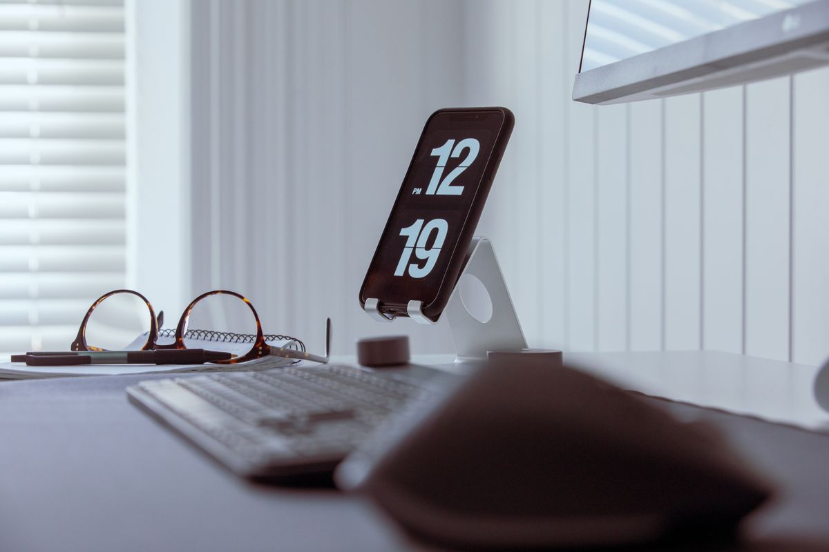 A desk clock showing the time beside a keyboard and a pair of glasses