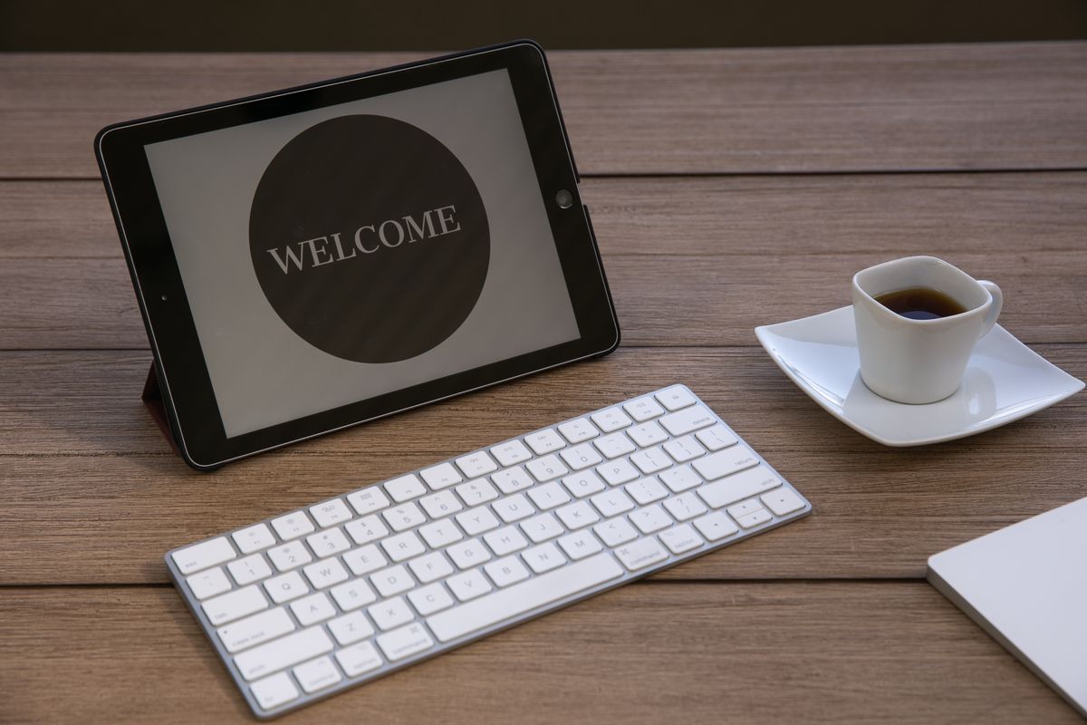 A desk with a tablet reading Welcome next to a keyboard and espresso