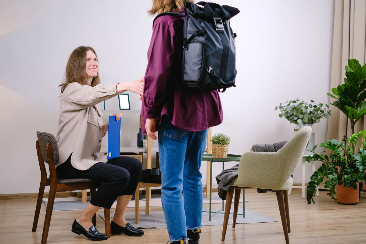 A smiling professional reaches out to welcome a new client into a warm office