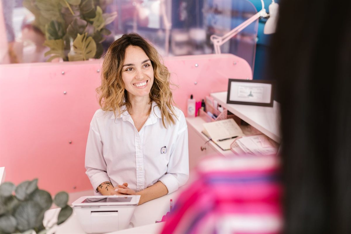 A smiling receptionist welcomes a returning client at a bright front desk