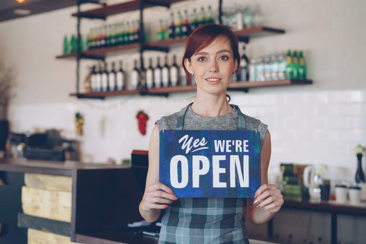 A cafe owner holds a hand painted sign reading yes we are open