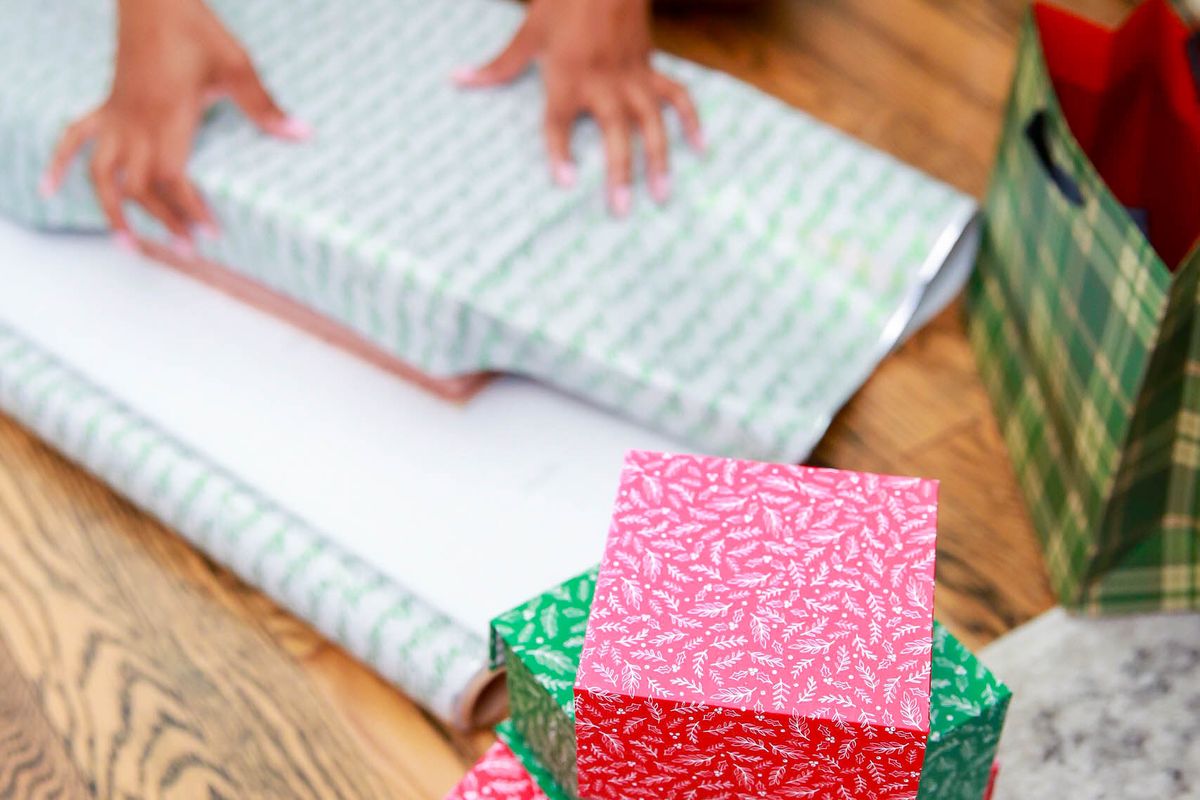 Hands wrapping Christmas gifts on a wooden table