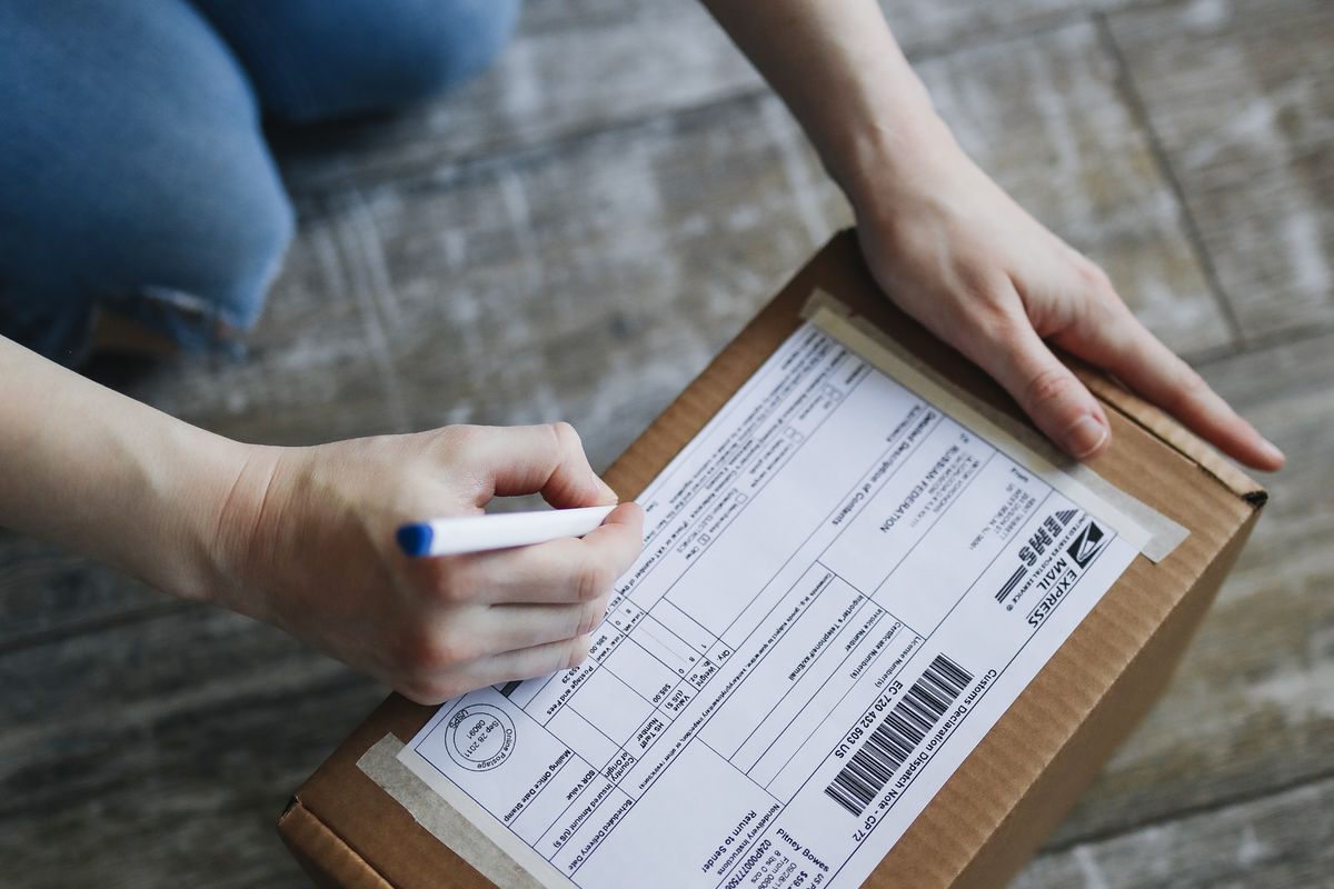 A hand filling in a shipping label on a parcel going abroad
