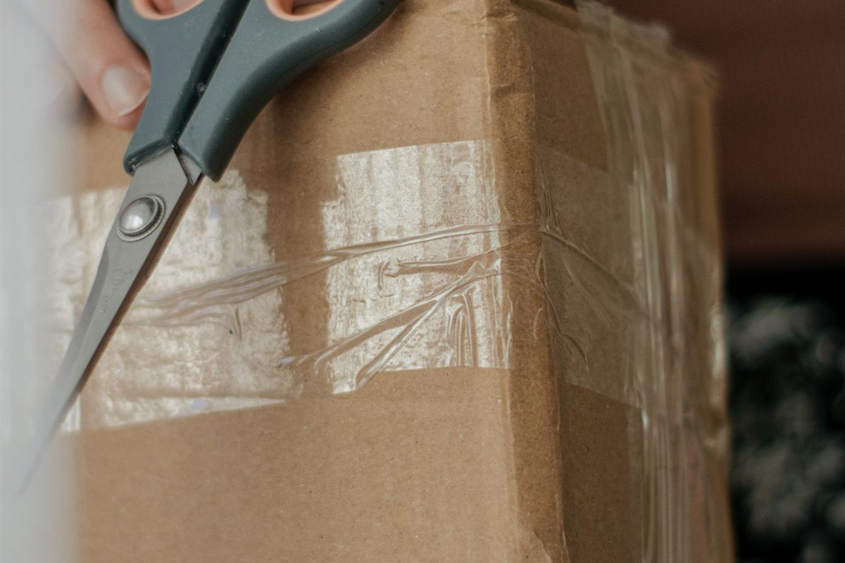 A person opens a taped cardboard parcel with scissors